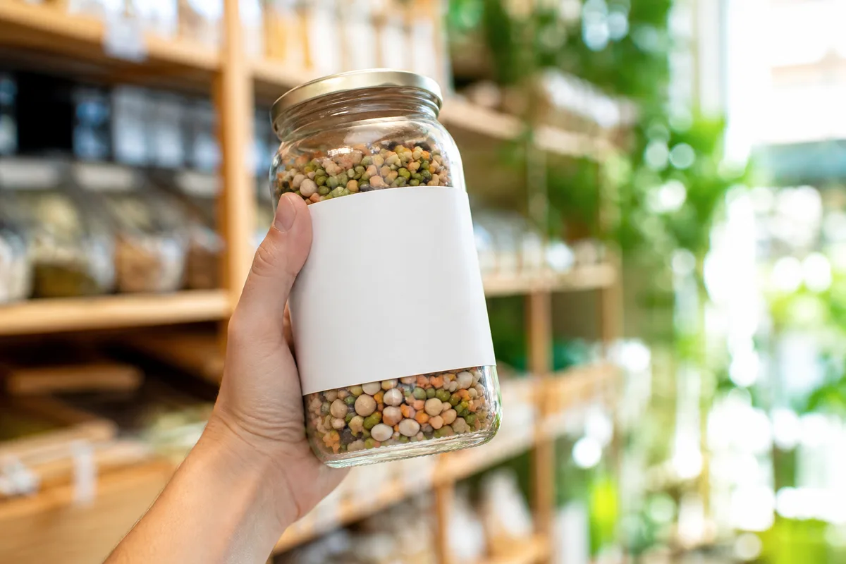 Main tenant un bocal alimentaire devant un rayon d&rsquo;épicerie biologique lumineux